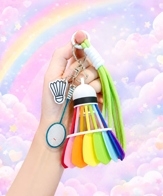 Hand holding a lime green badminton shuttlecock rope keychain against a pastel rainbow cloud background