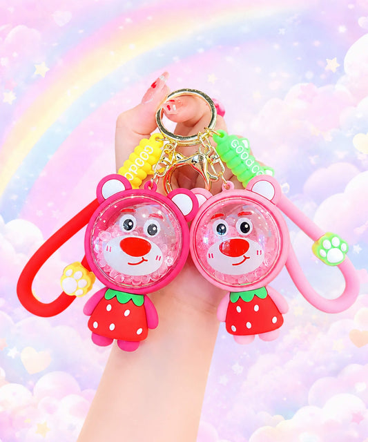 Strawberry Bear bead shaker keychains in red and pink colour options held in hand with a pastel rainbow background