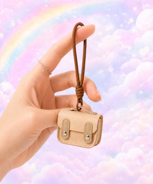 Hand holding a beige mini PU leather earphone pouch keychain against a pastel rainbow cloud background