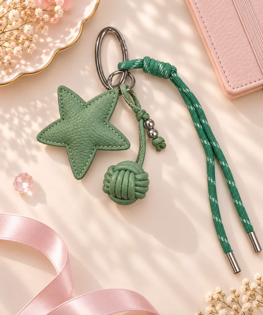 Green star PU leather bag charm keychain with rope knot detail on a soft pink background