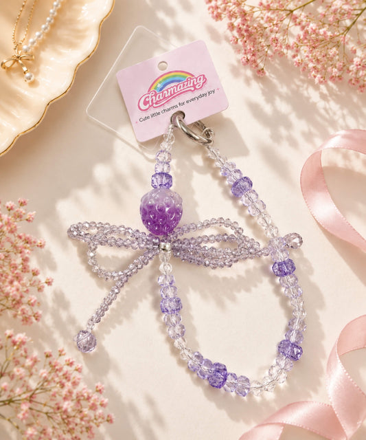 Purple strawberry bow beaded phone charm styled in a soft pastel lifestyle setting