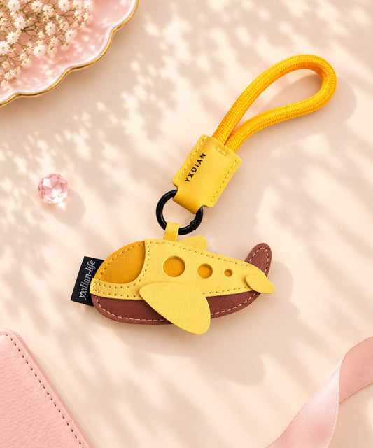 Yellow airplane PU leather bag charm keychain styled on a soft pink neutral background