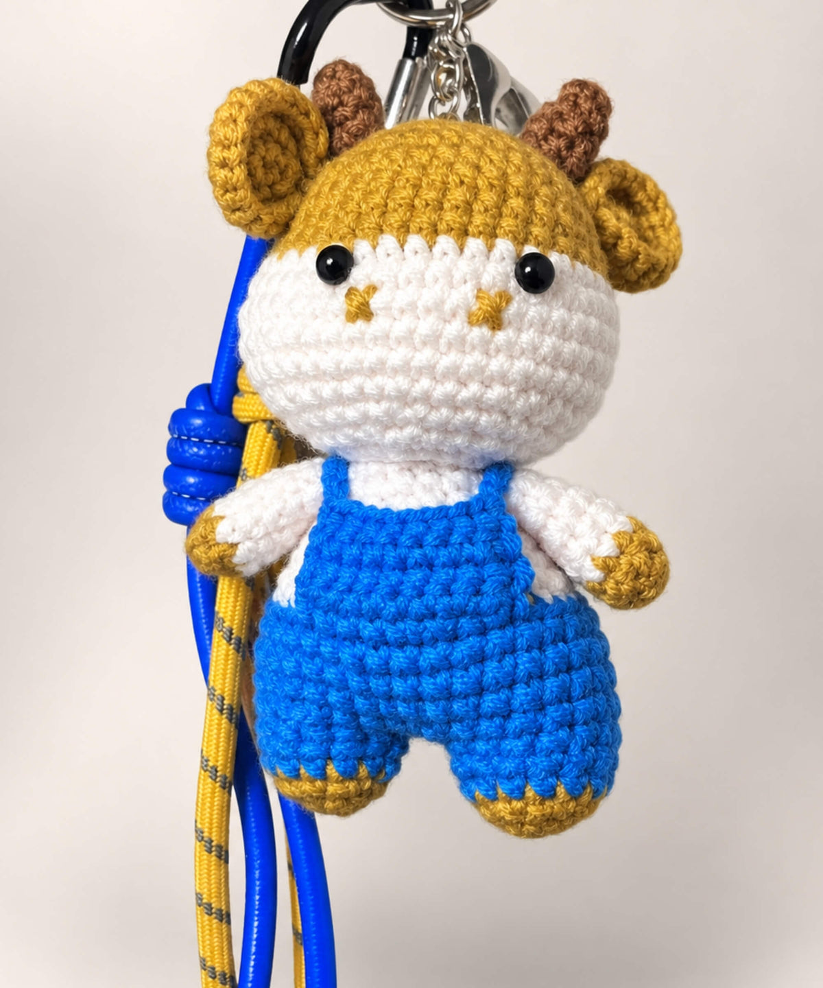 Close-up of horned cow crochet keychain wearing blue overalls