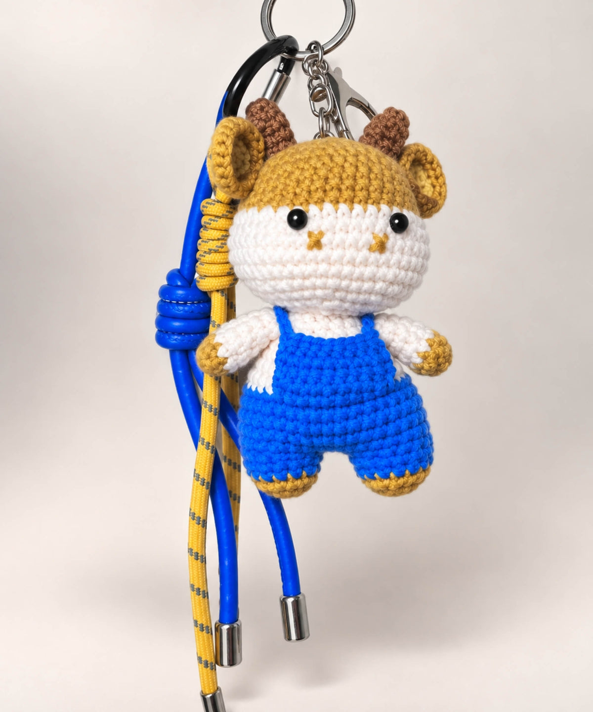 Horned cow crochet keychain wearing blue overalls with yellow and blue hanging cords