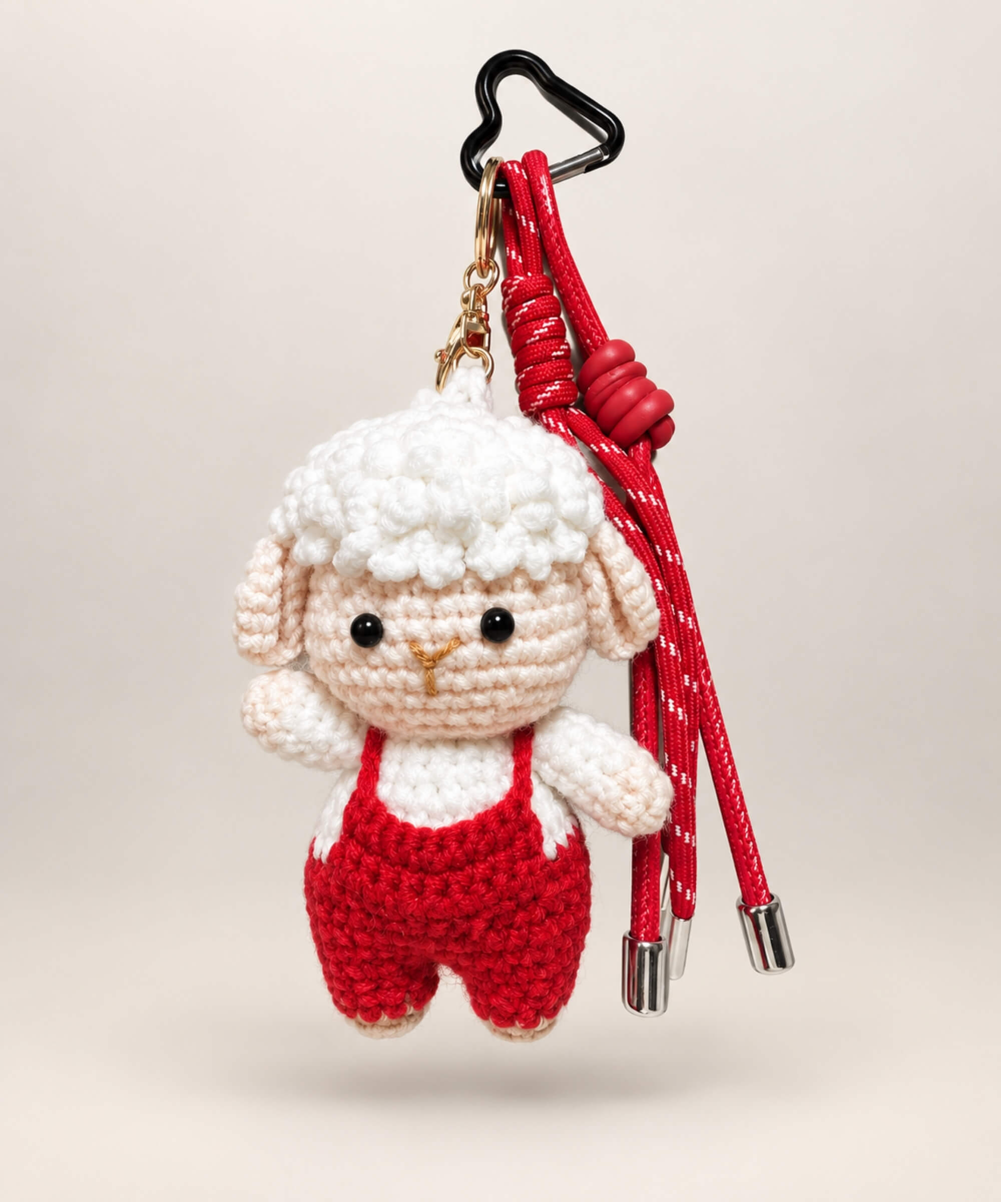 Lamb crochet keychain wearing red overalls with red hanging cords