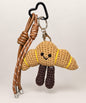 Golden brown croissant bakery crochet keychain with smiling face and brown straps