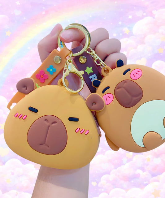 Capybara silicone coin purse keychains with two cute brown designs held in hand, mini wallet pouch bag charm with pastel background