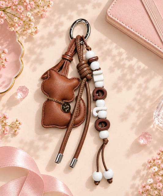 Brown cat PU leather bag charm keychain with beaded cord detail on a soft pink background
