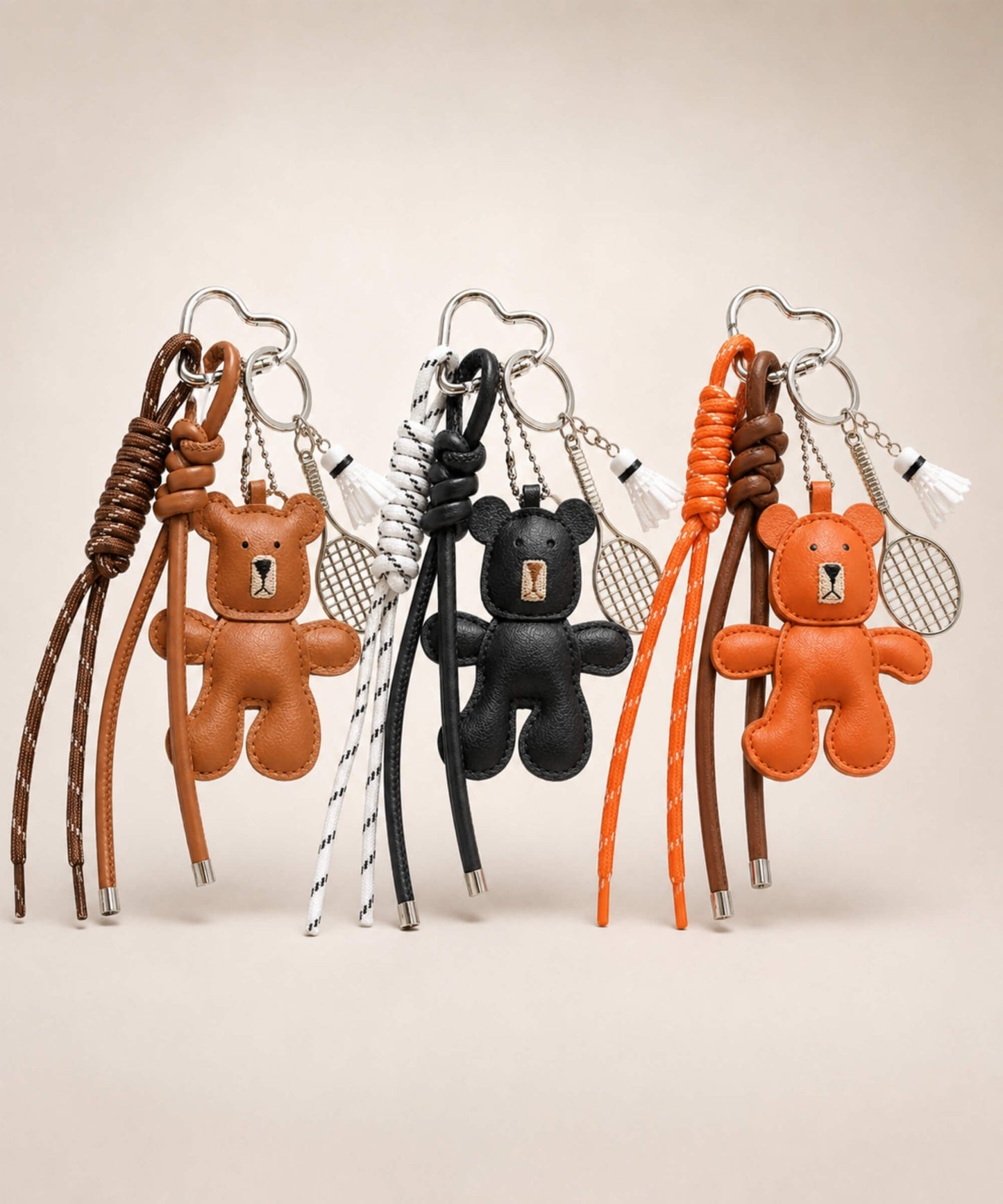 Brown, black and orange bear PU leather bag charm keychains with badminton racket charms and shuttlecock charms displayed together on a neutral background.