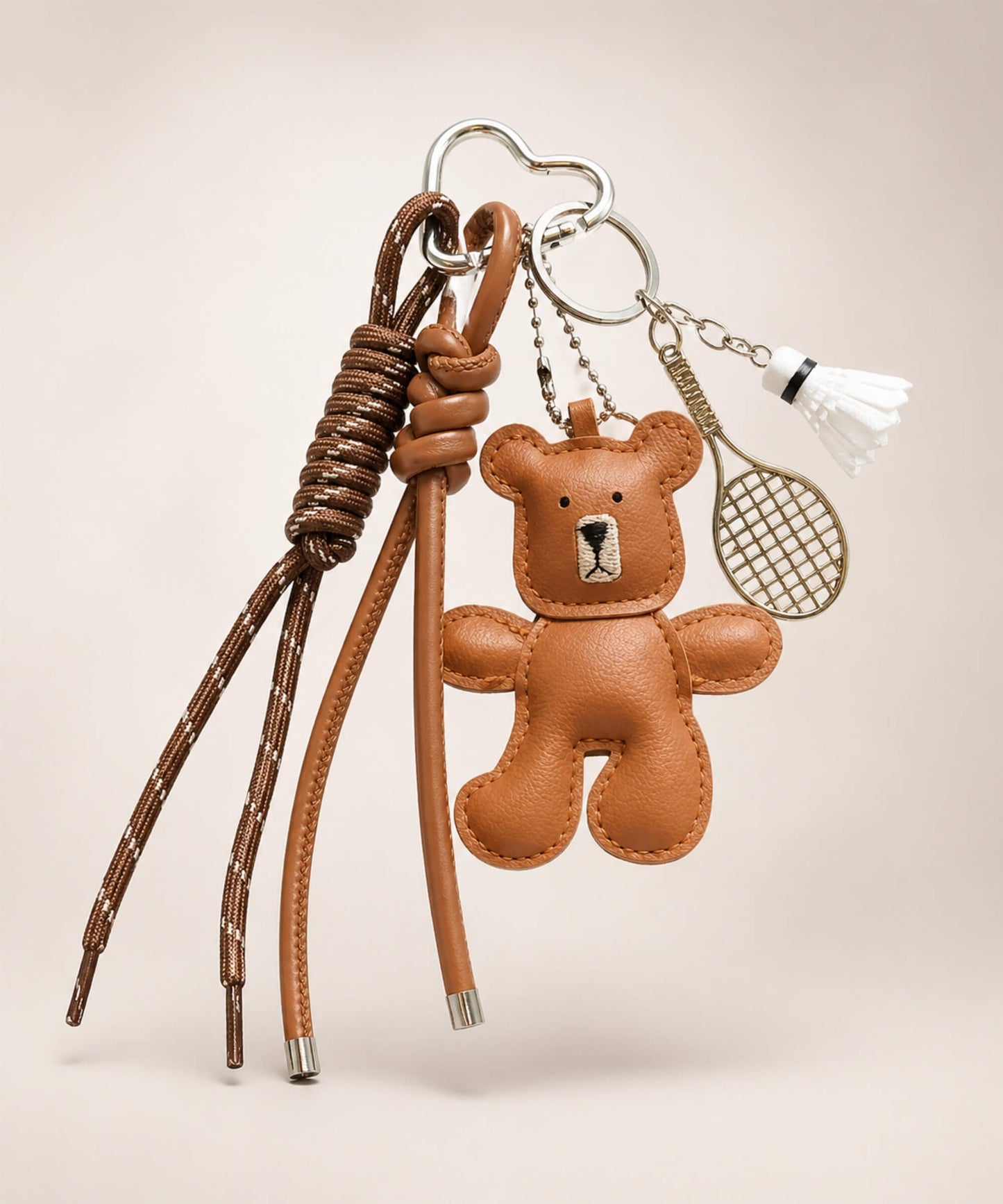 Brown bear PU leather bag charm keychain with a badminton racket charm and shuttlecock charm on a neutral background.