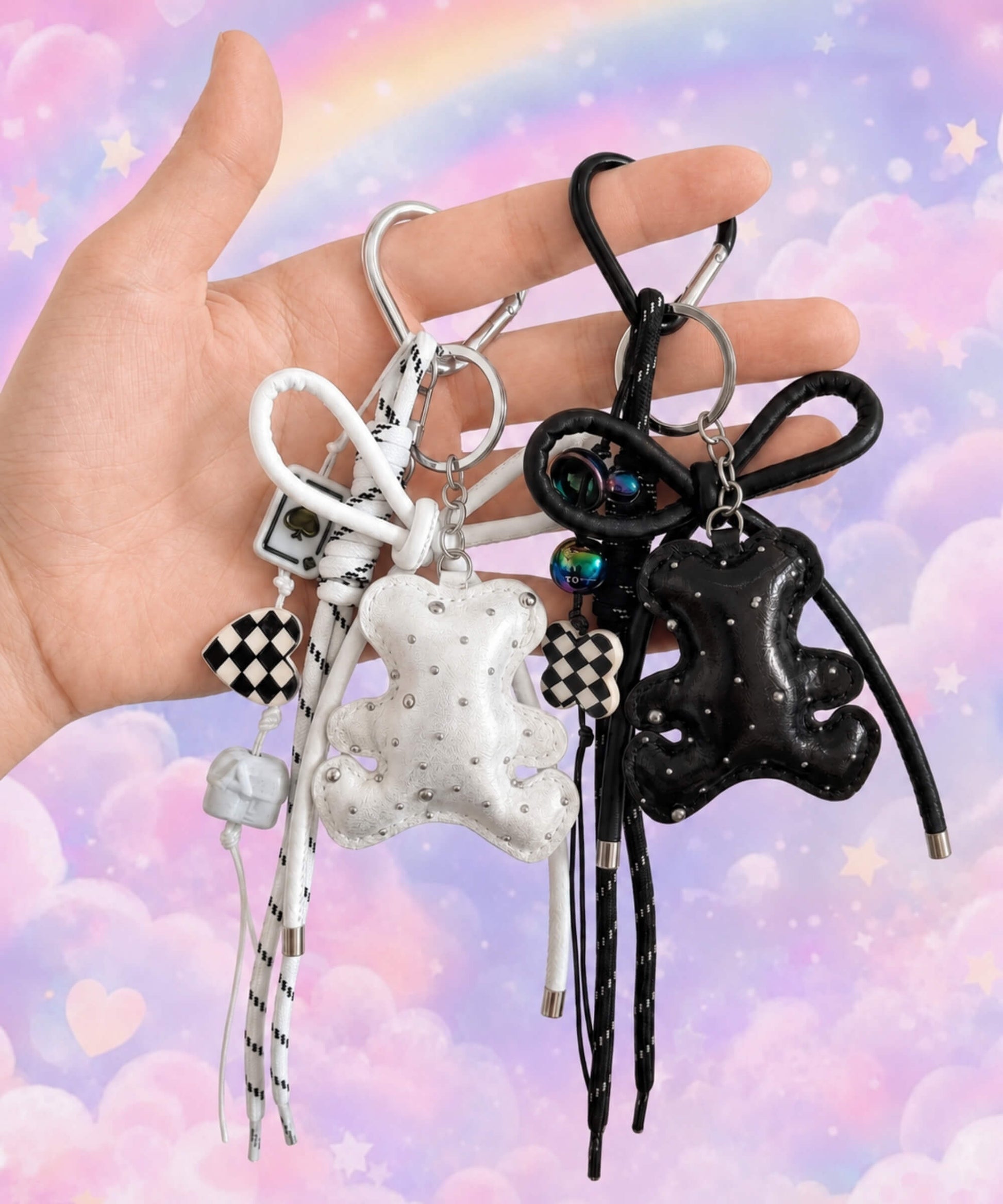 Hand holding white and black bear PU leather bag charm keychains with sparkle charms and decorative hanging charms against a pastel rainbow background.