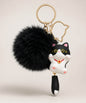 Black cat pom pom resin keychain with fluffy plush ball and gold hardware on a neutral background