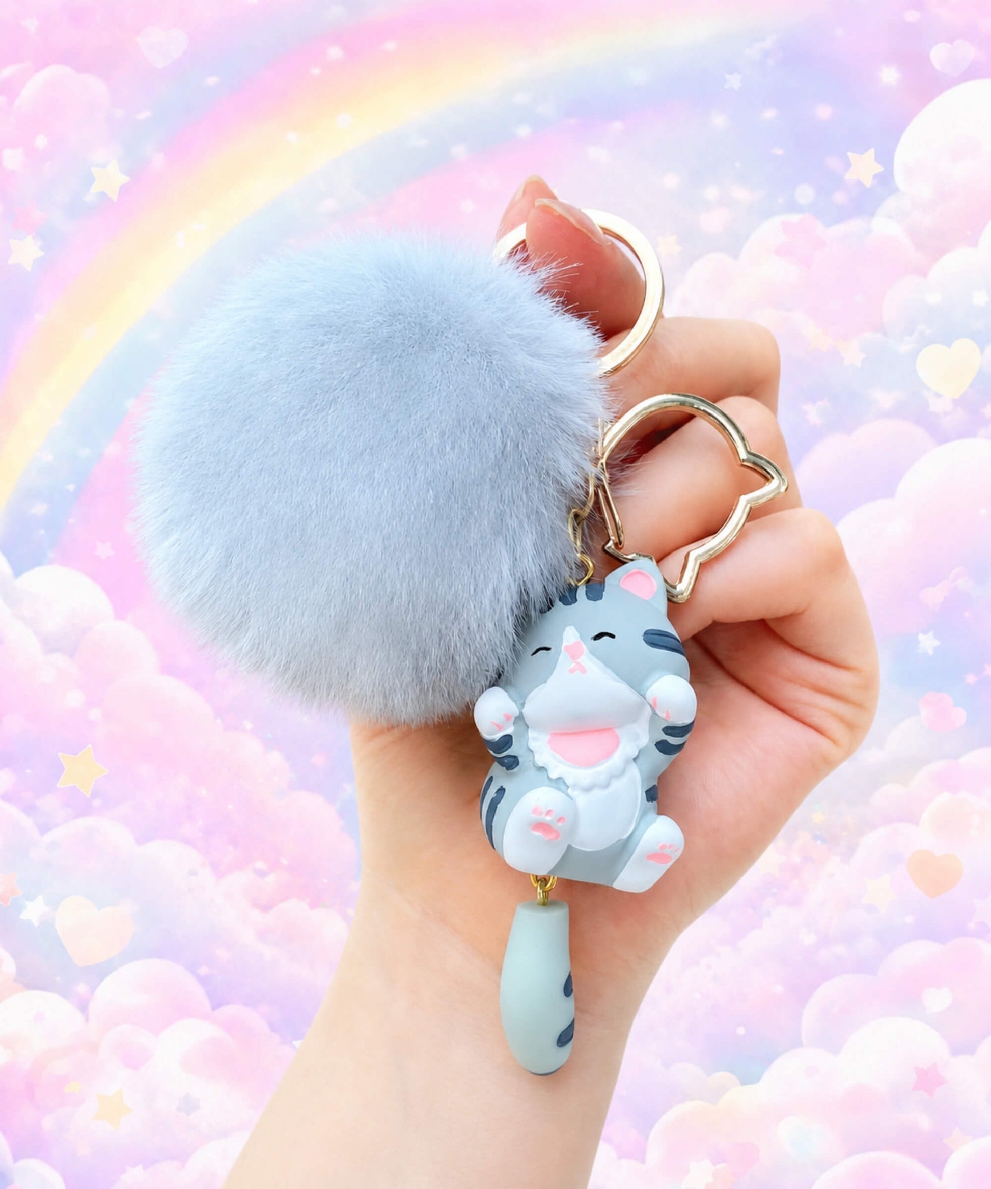 Blue cat pom pom resin keychain held in hand with a pastel rainbow background