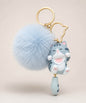 Blue cat pom pom resin keychain with fluffy plush ball and gold hardware on a neutral background