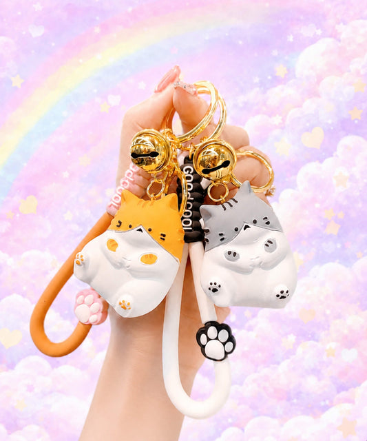 Hand holding orange and grey chubby cat resin keychains against a pastel rainbow background.