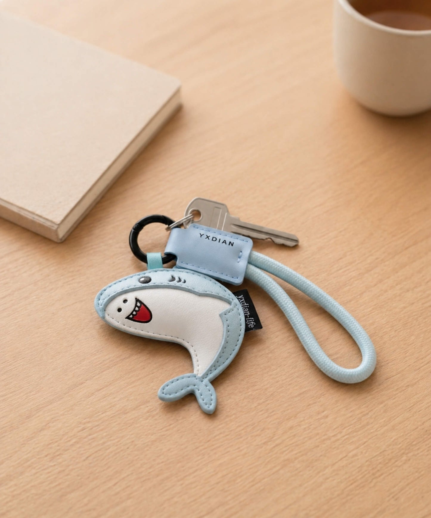 Blue cute shark PU leather keychain attached to keys on a wooden table in a lifestyle setting.