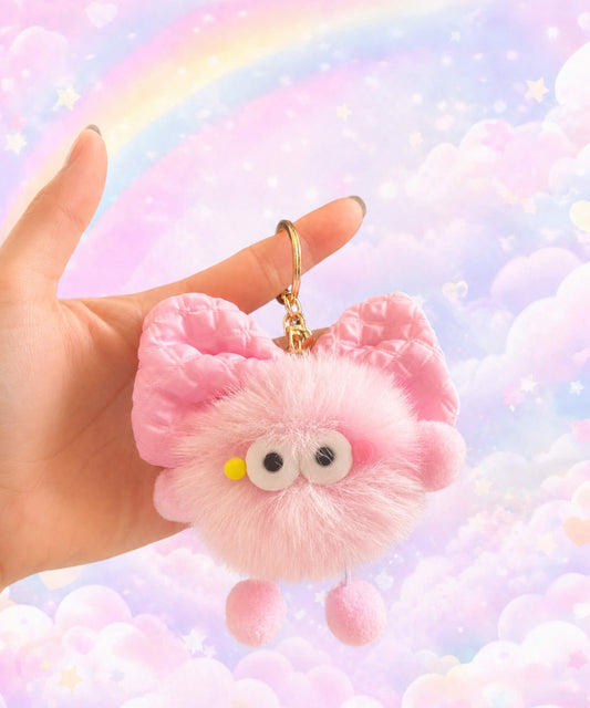 Fluffy bow plush keychain held in hand with soft pink plush texture and pastel rainbow cloud background