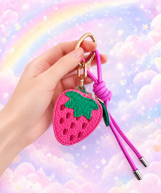 Strawberry fruit coin purse keychain held in hand with pink strap and pastel rainbow cloud background