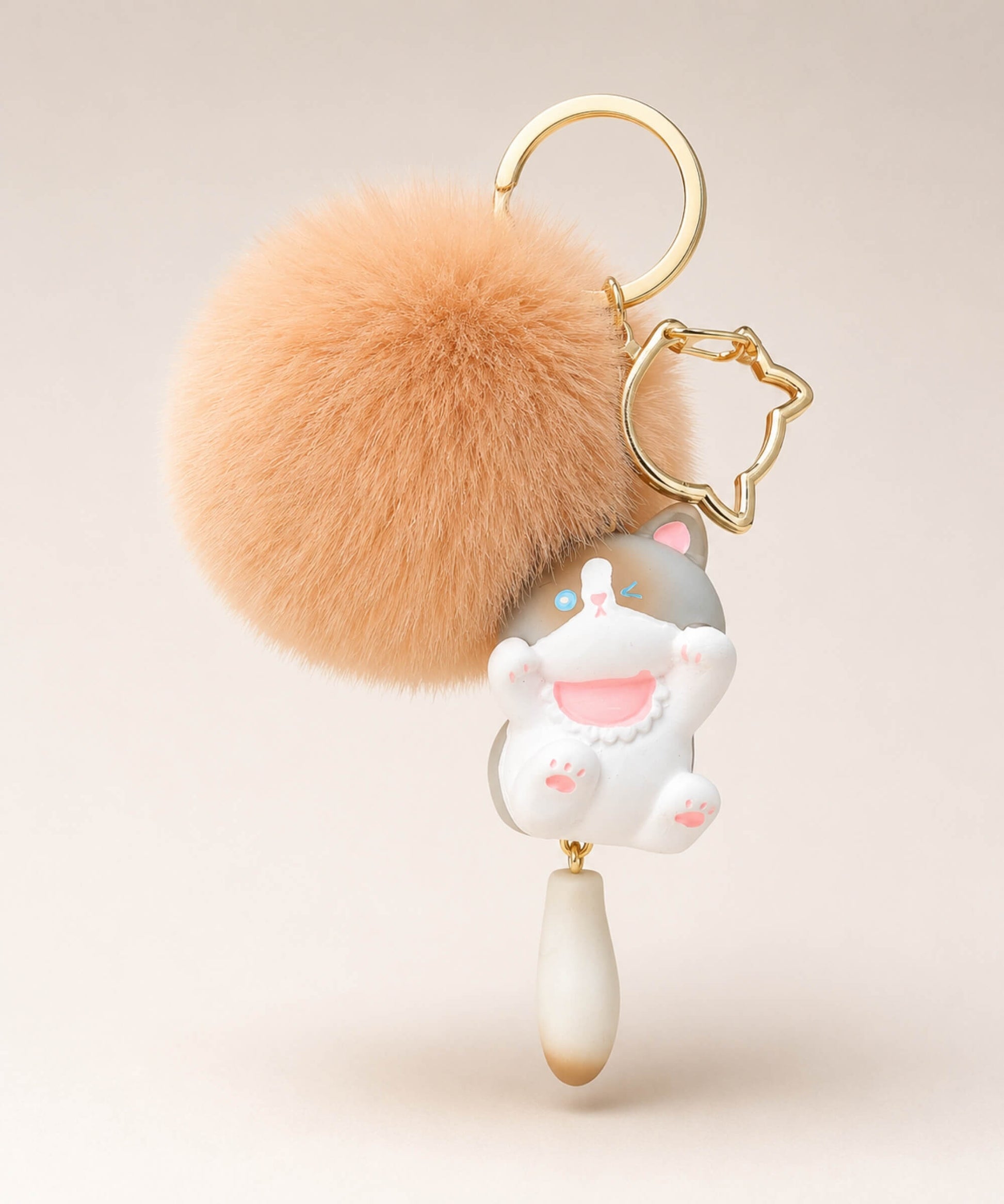 Grey cat pom pom resin keychain with peach fluffy plush ball and gold hardware on a neutral background