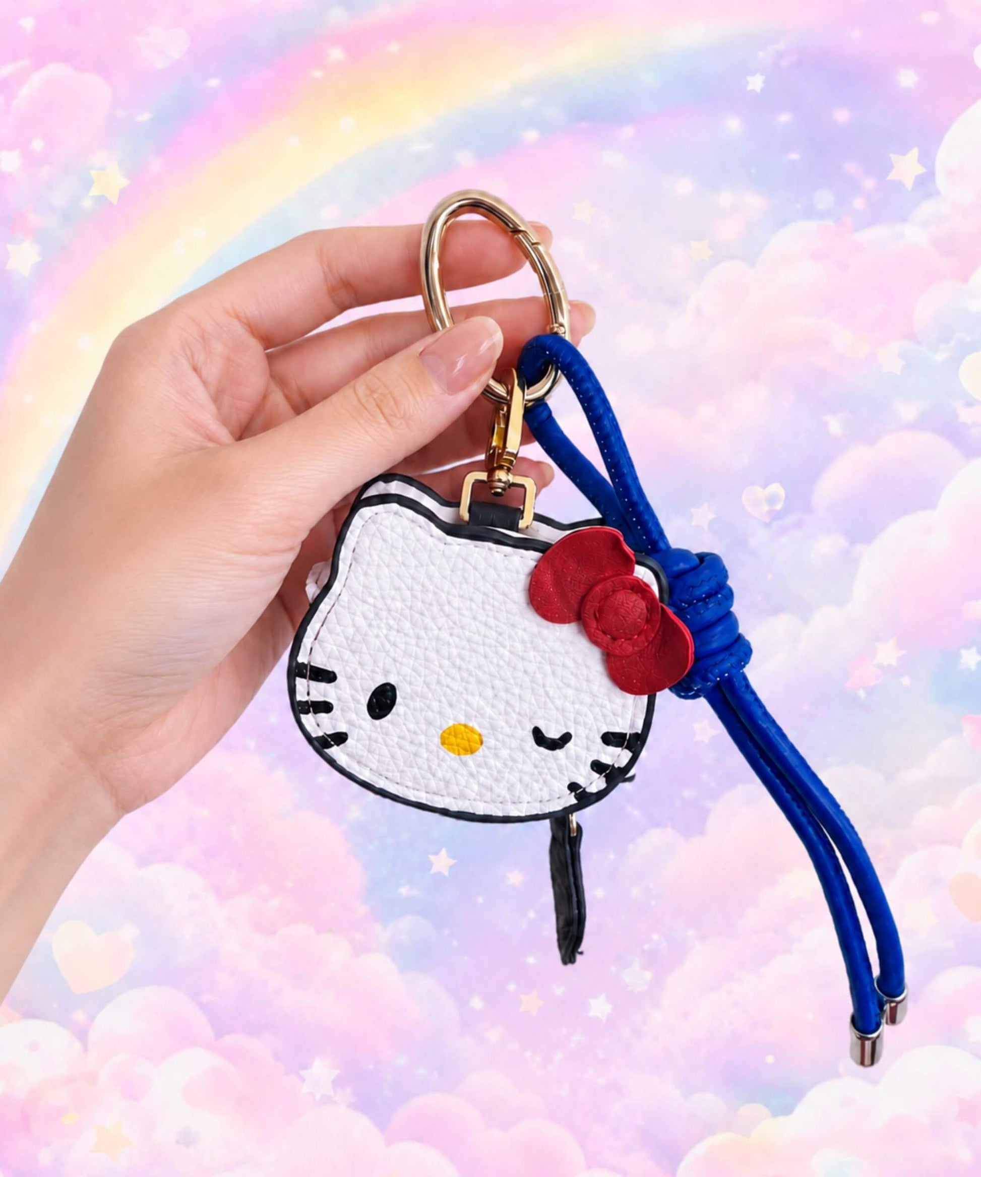 Hello Kitty coin purse keychain held in hand with blue strap and pastel rainbow cloud background