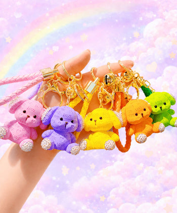 Hand holding pink, purple, yellow, orange and green love puppy resin keychains against a pastel rainbow background.