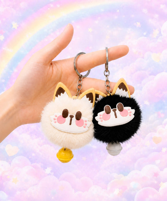 Cream and black lucky cat bell plush keychains held by hand on a pastel rainbow background