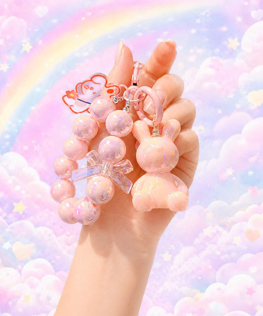 Pink bunny beaded keychain held in hand with a pastel rainbow background