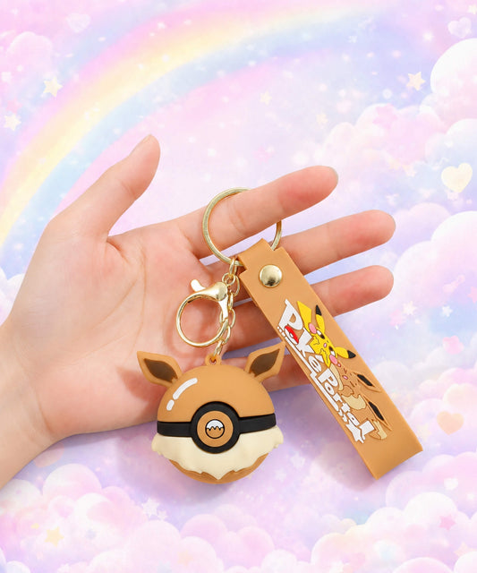 Brown Poke Ball-inspired strap keychain held in hand with matching wrist strap and pastel rainbow cloud background
