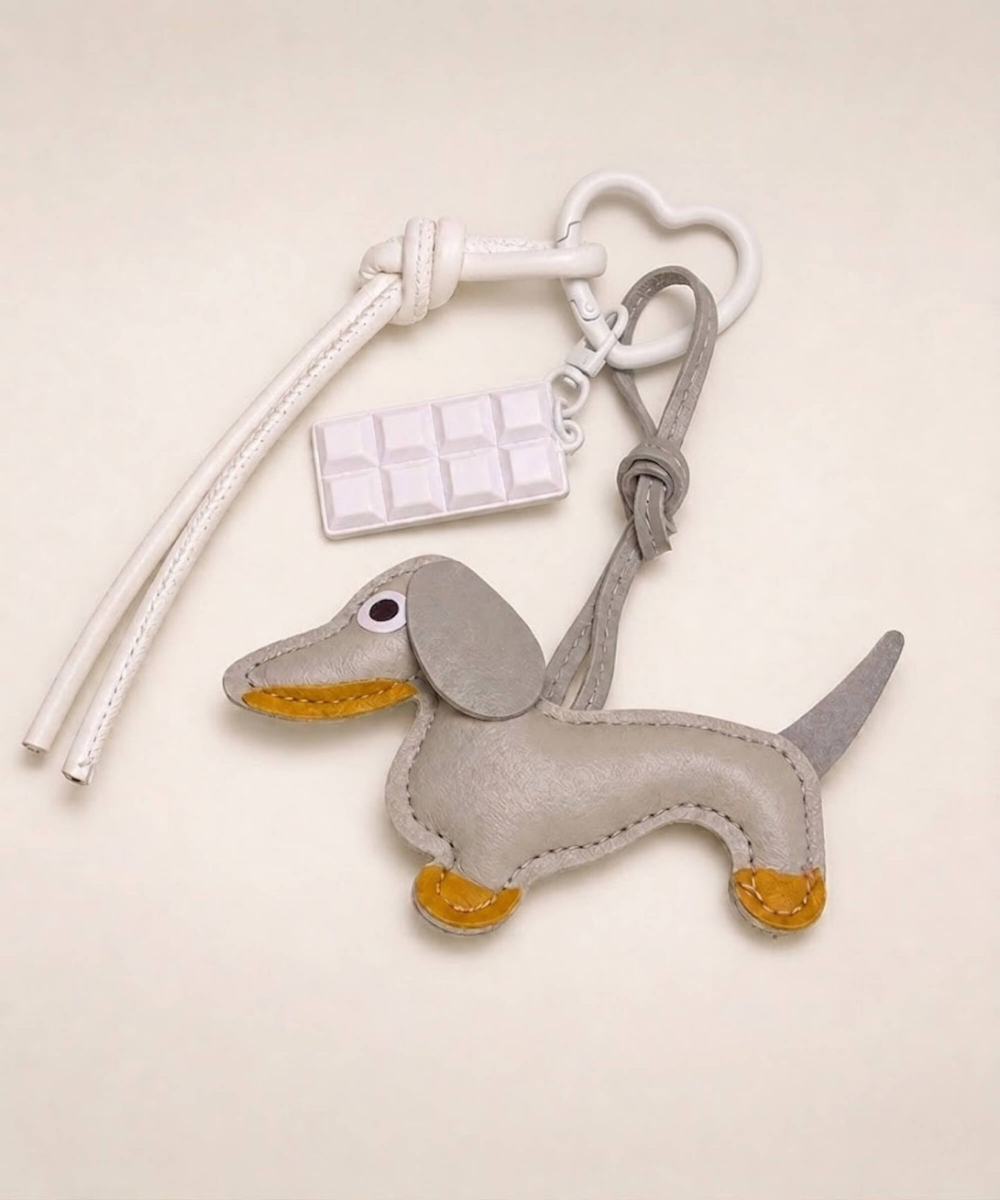Grey sausage dog PU leather bag charm keychain with a white chocolate charm styled on a neutral background.