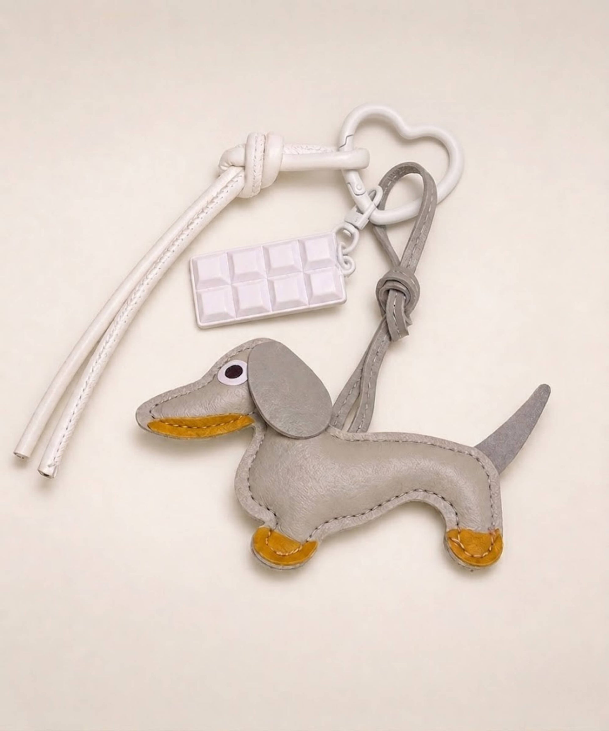 Grey sausage dog PU leather bag charm keychain with a white chocolate charm styled on a neutral background.