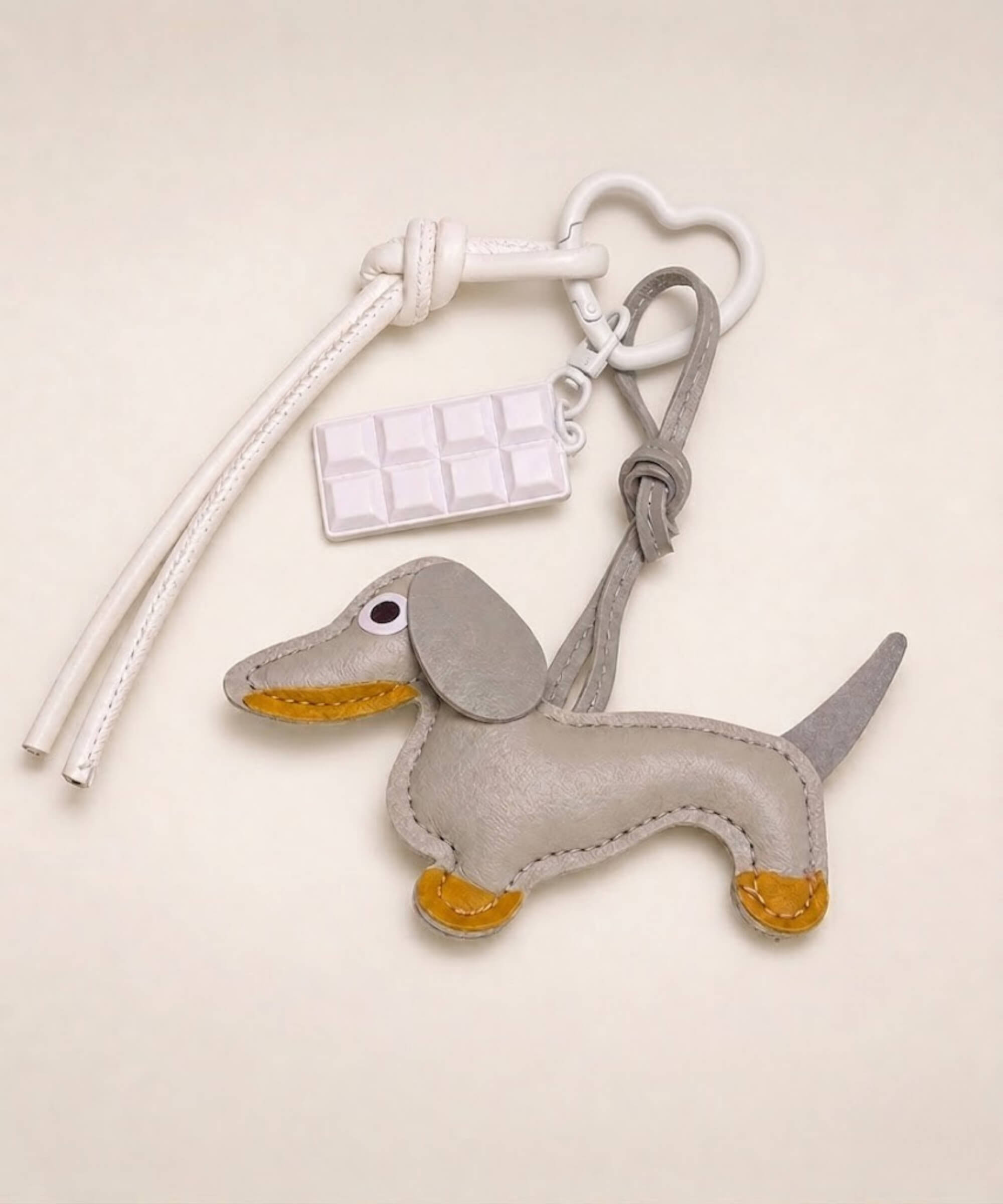 Grey sausage dog PU leather bag charm keychain with a white chocolate charm styled on a neutral background.