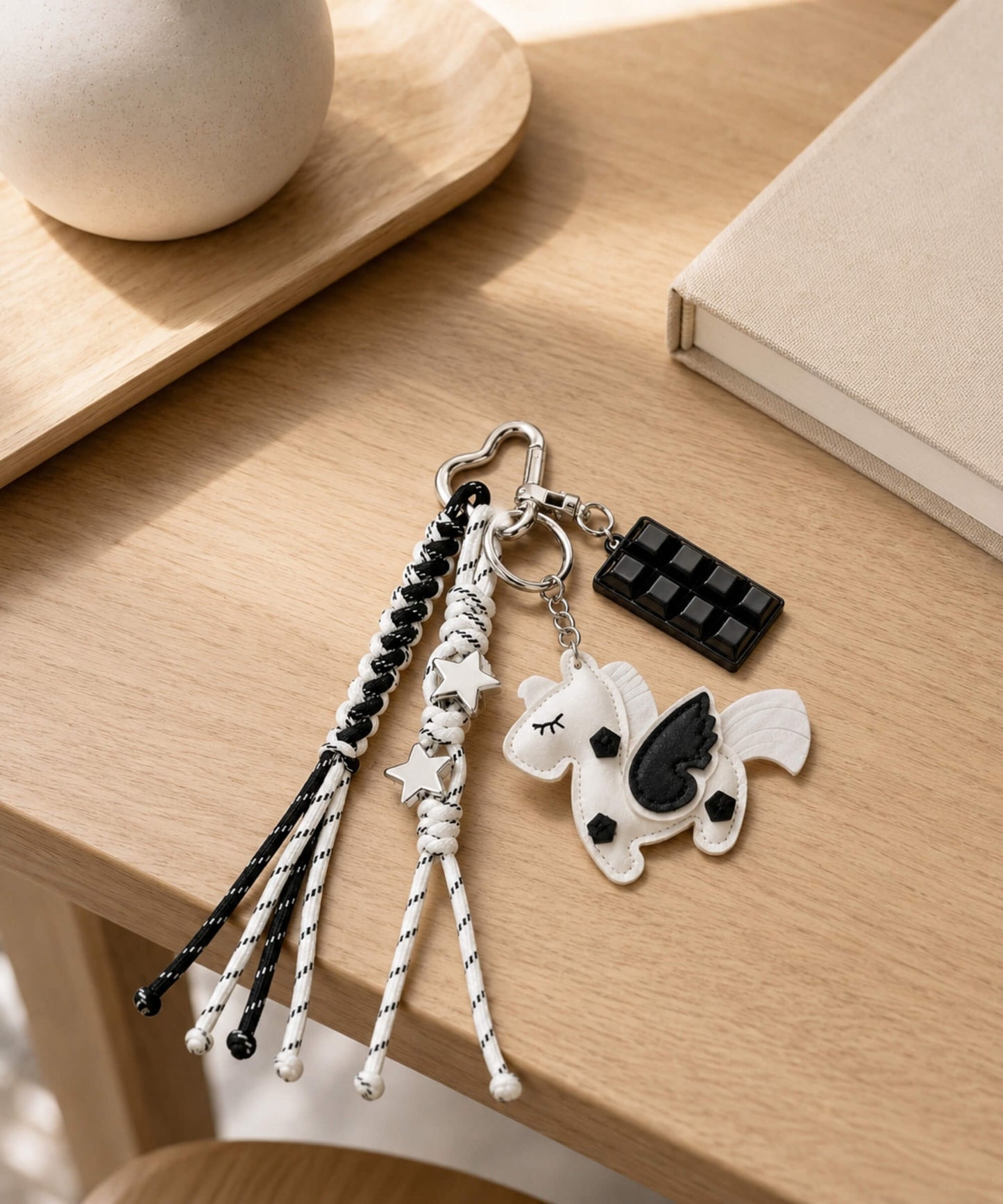 White unicorn PU leather bag charm keychain with star and chocolate charms on a wooden table.