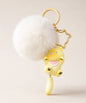Yellow cat pom pom resin keychain with white fluffy plush ball and gold hardware on a neutral background