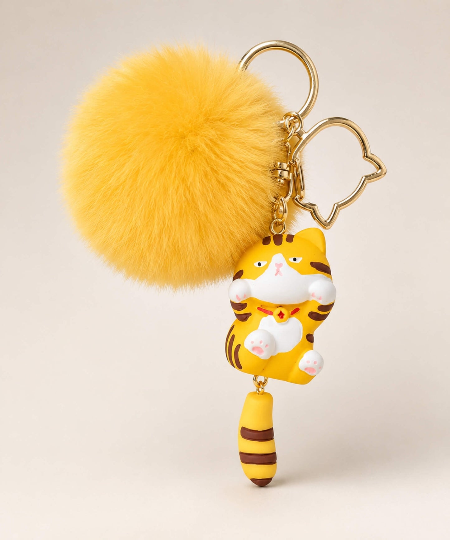 Yellow tabby cat pom pom resin keychain with fluffy plush ball and gold hardware on a neutral background
