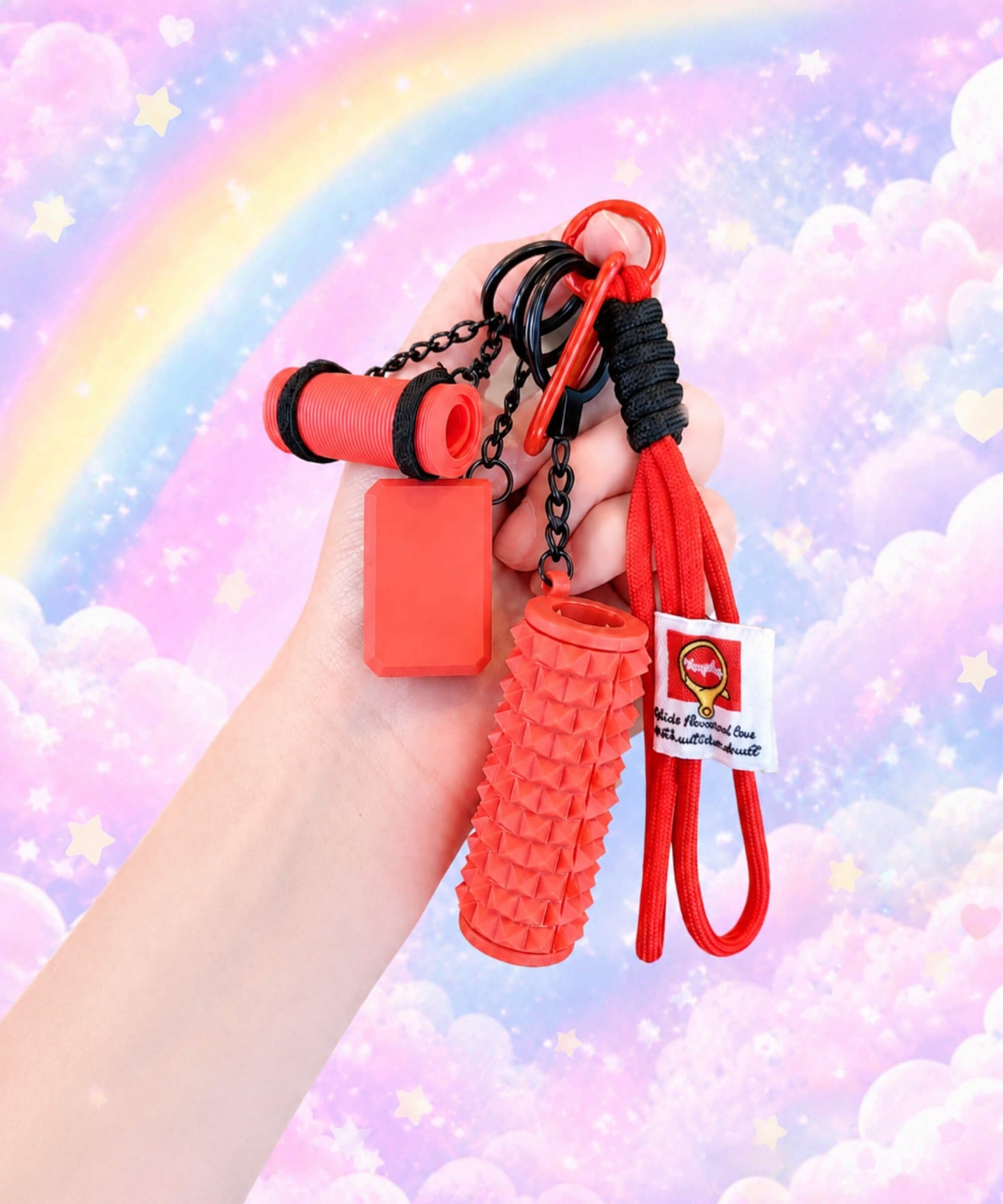 Hand holding a red yoga rope keychain with mini foam roller charm against a pastel rainbow cloud background