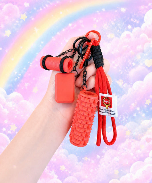Hand holding a red yoga rope keychain with mini foam roller charm against a pastel rainbow cloud background