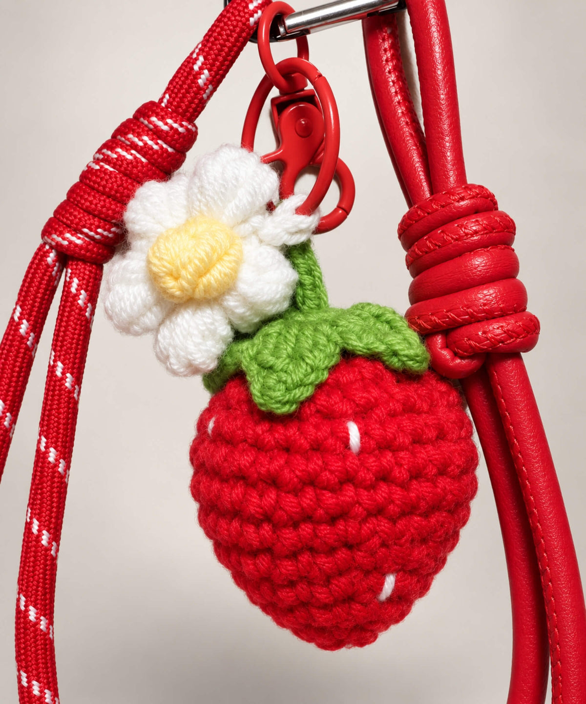 Close-up of strawberry crochet keychain with white flower green leaves and red cord details