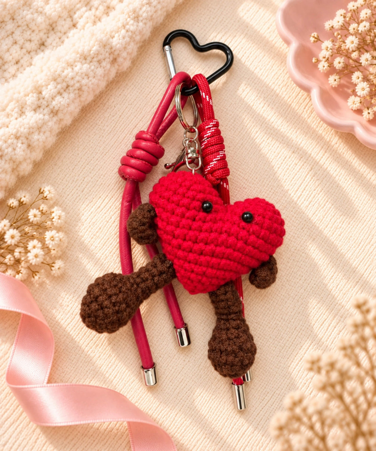 Red heart character crochet keychain styled on a warm neutral fabric background