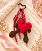 Red heart character crochet keychain styled on a warm neutral fabric background
