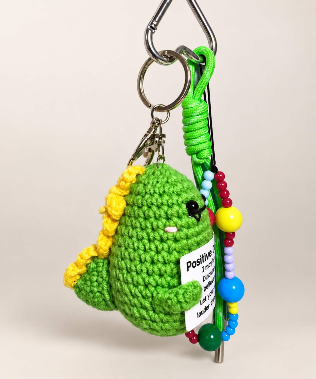 Side view of green Positive Dinosaur crochet keychain with yellow crochet spikes and bead charm