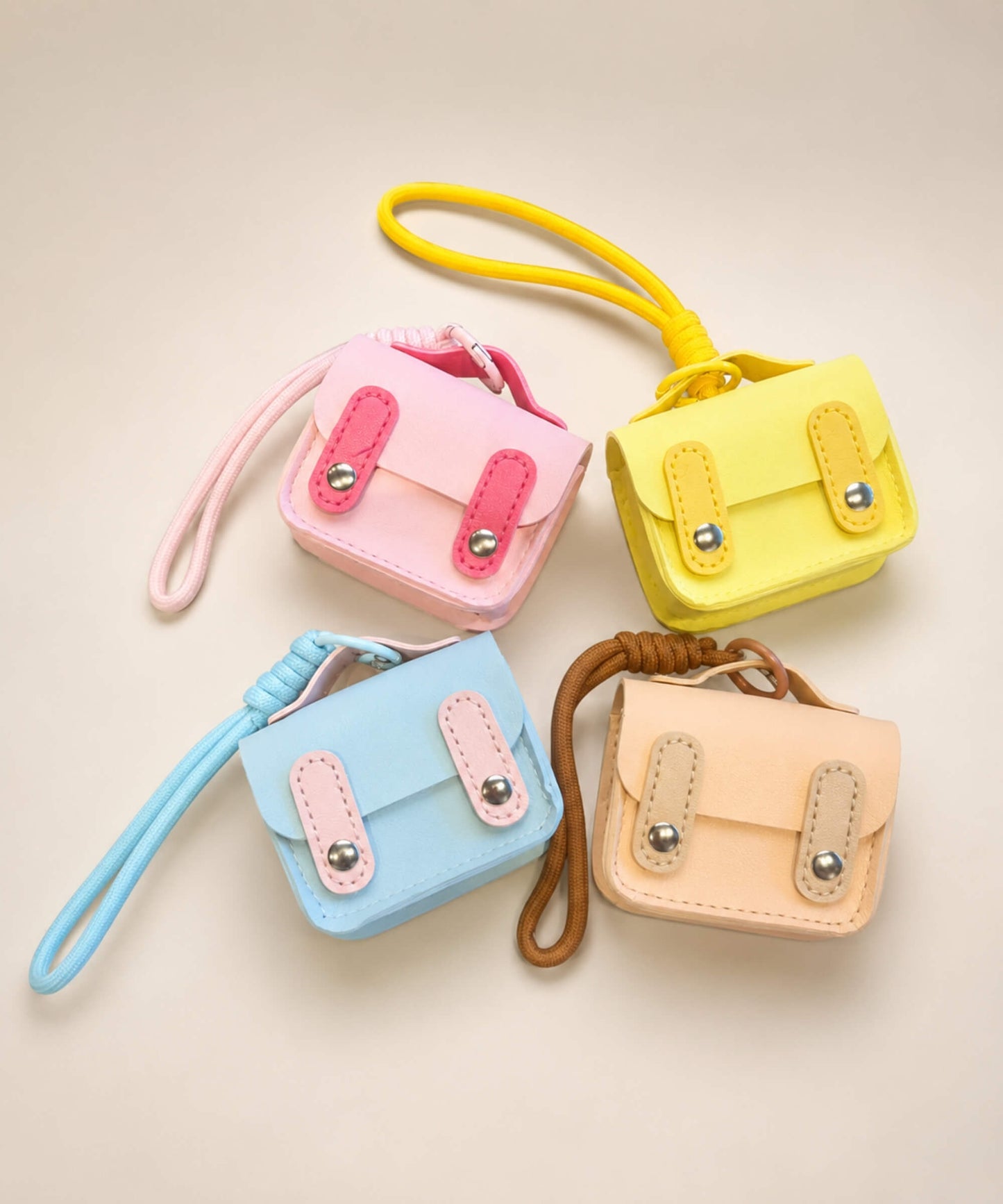 Mini PU leather earphone pouch keychains in pink, yellow, blue and beige displayed together on a neutral background