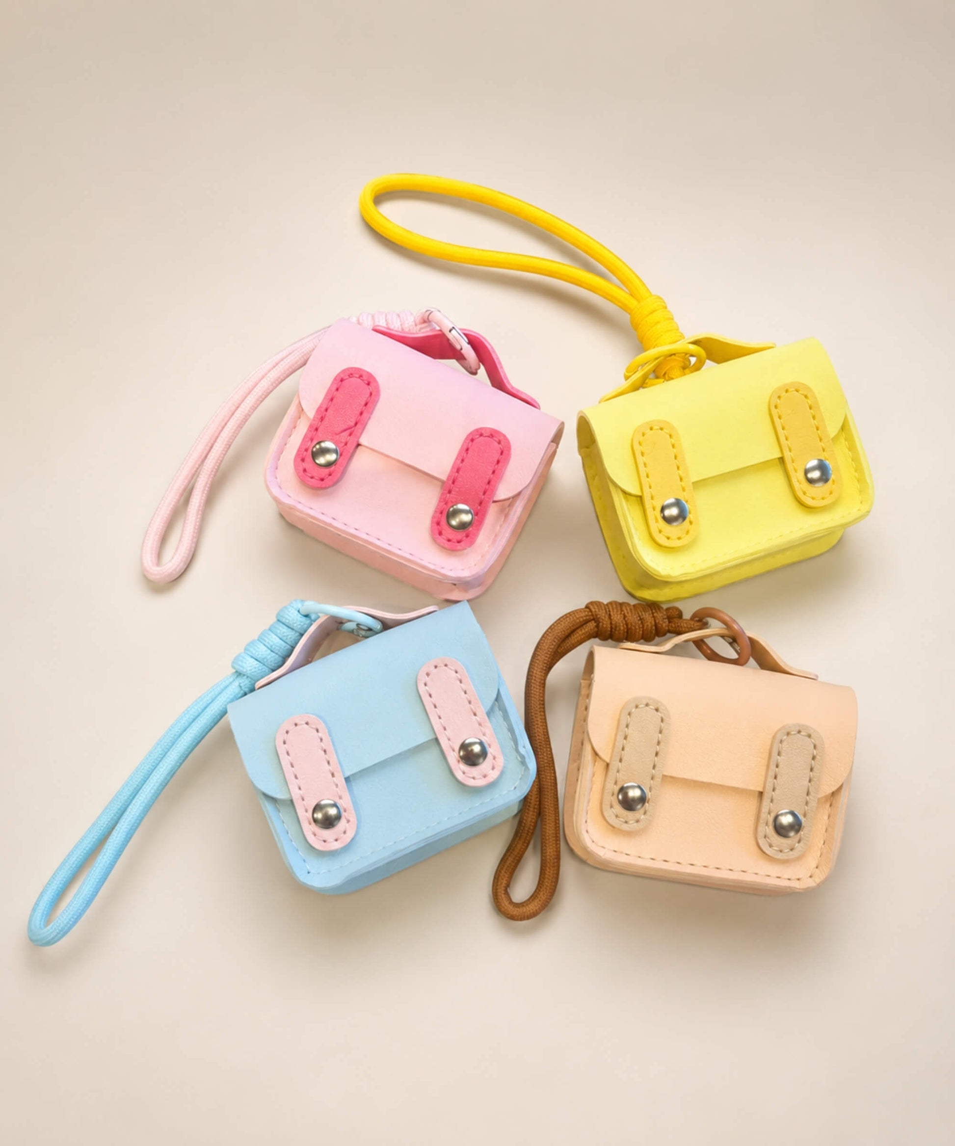 Mini PU leather earphone pouch keychains in pink, yellow, blue and beige displayed together on a neutral background