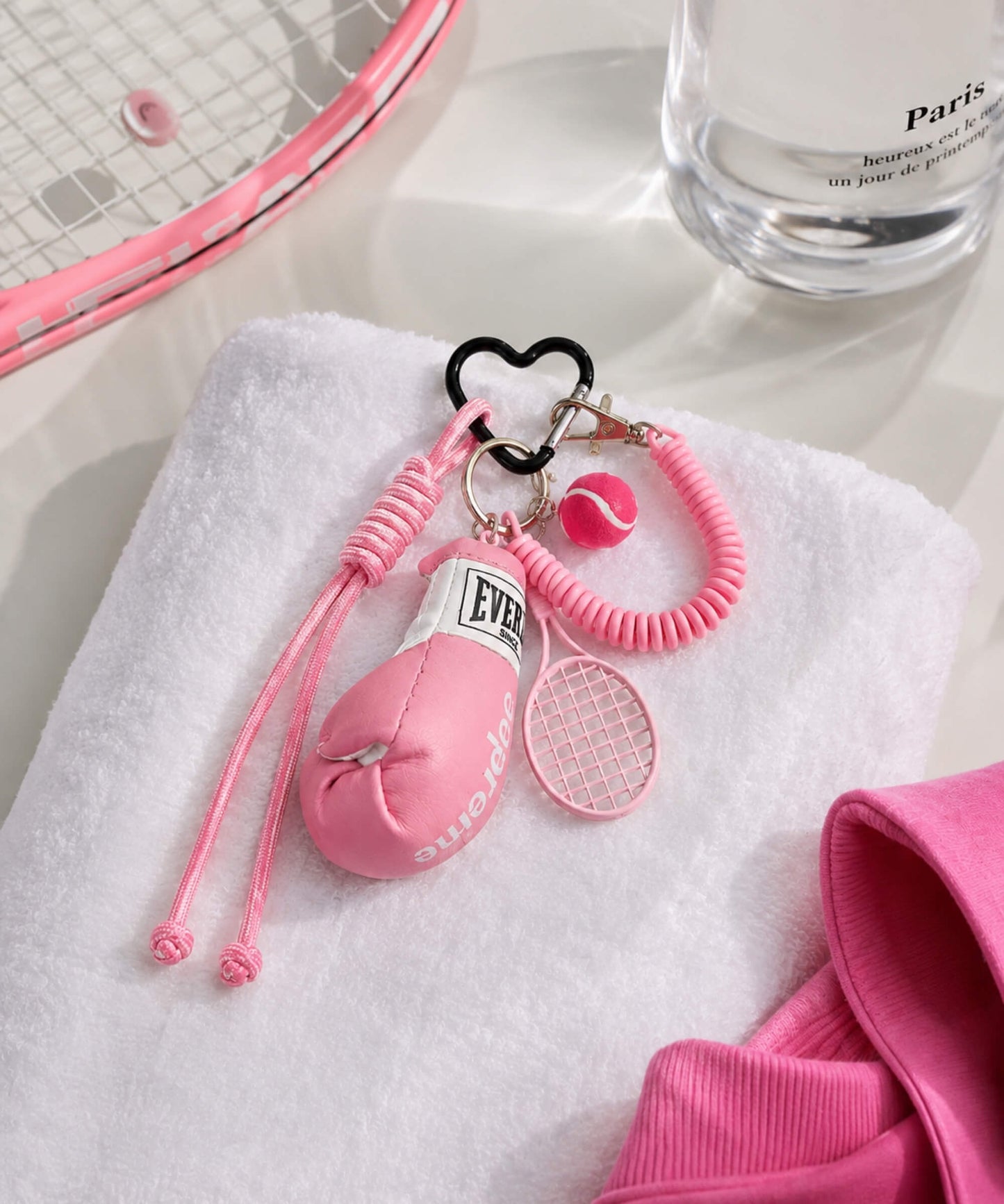 Pink boxing glove and tennis rope keychain styled on a white towel with tennis racket and bottle