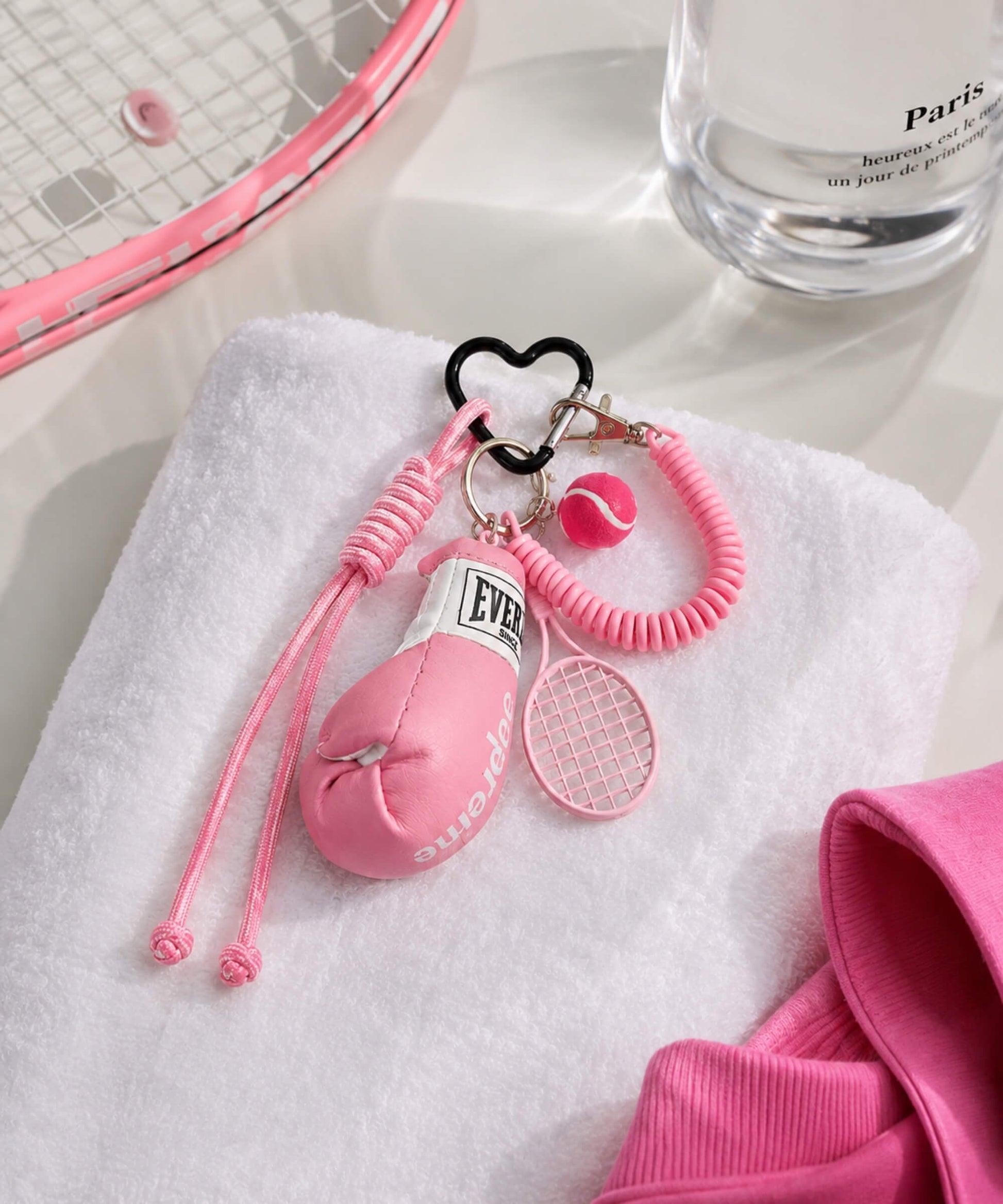 Pink boxing glove and tennis rope keychain styled on a white towel with tennis racket and bottle