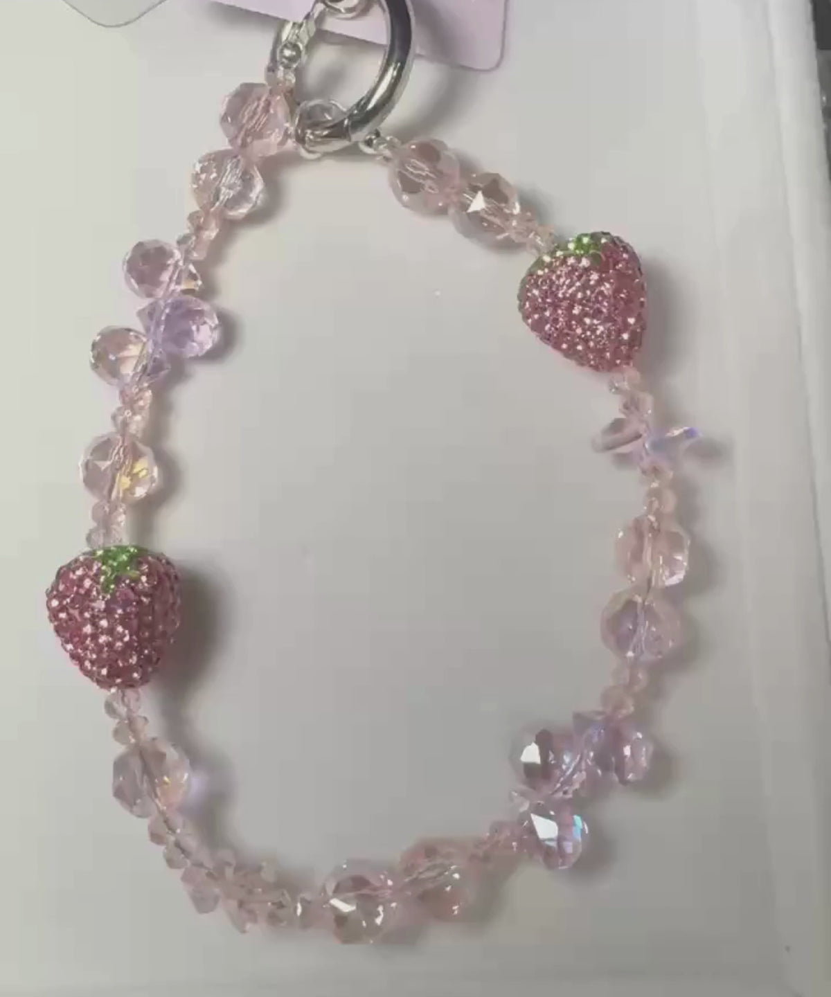 Video of a strawberry beaded phone charm featuring crystal-style beads and sparkling strawberry details by CHARMAZIN