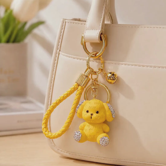 Yellow love puppy resin keychain hanging from a cream handbag in a lifestyle setting.
