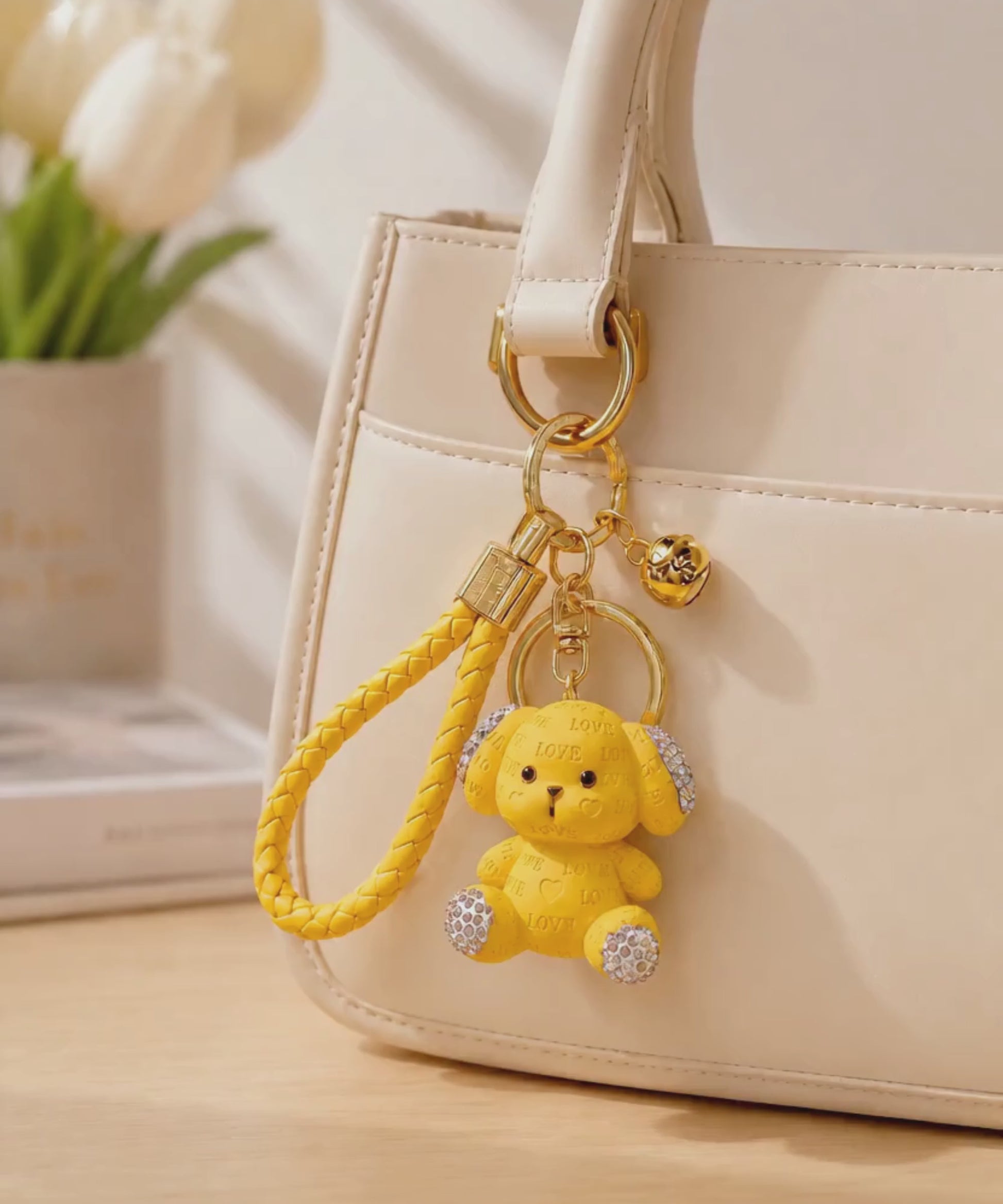 Yellow love puppy resin keychain hanging from a cream handbag in a lifestyle setting.