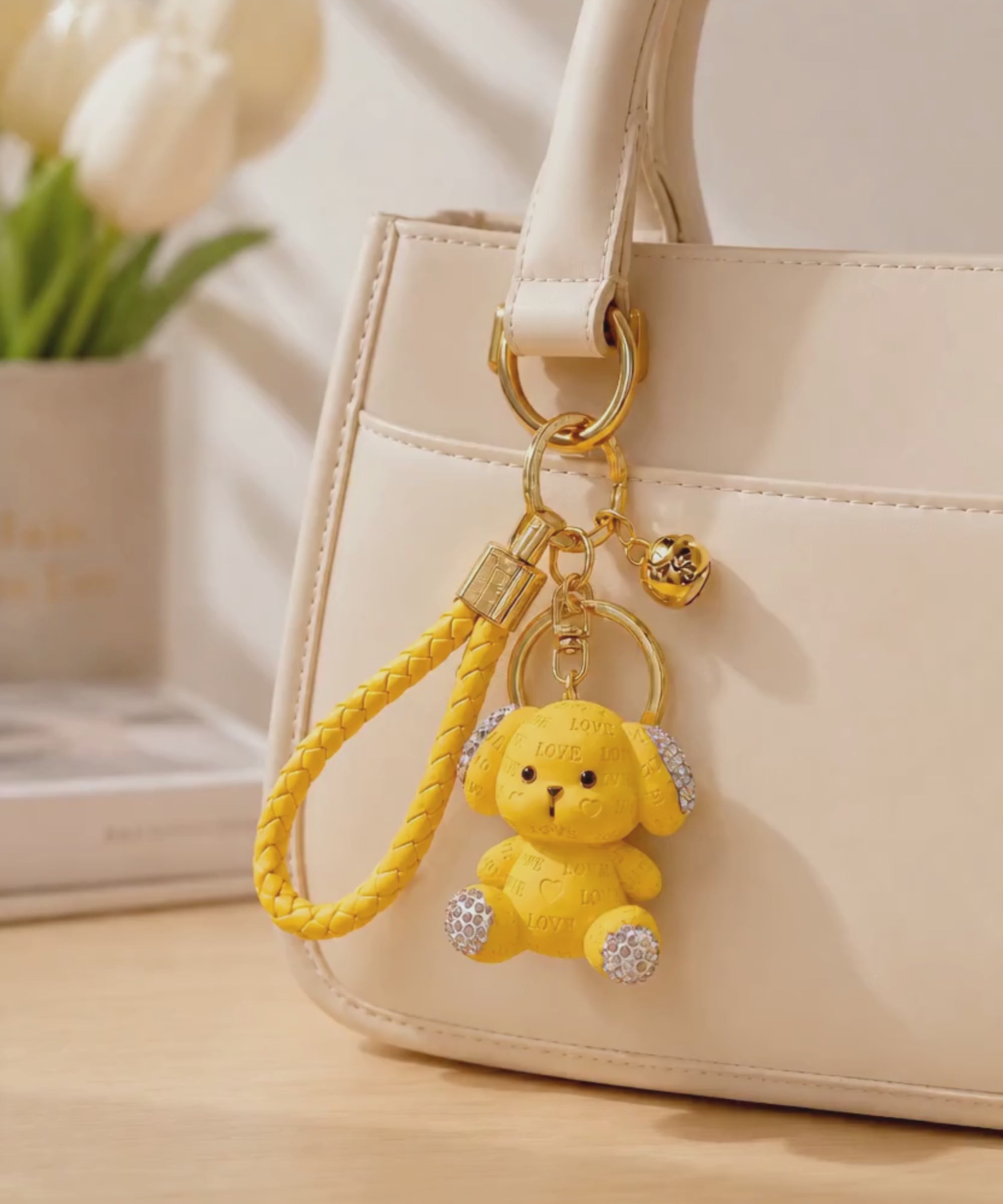 Yellow love puppy resin keychain hanging from a cream handbag in a lifestyle setting.