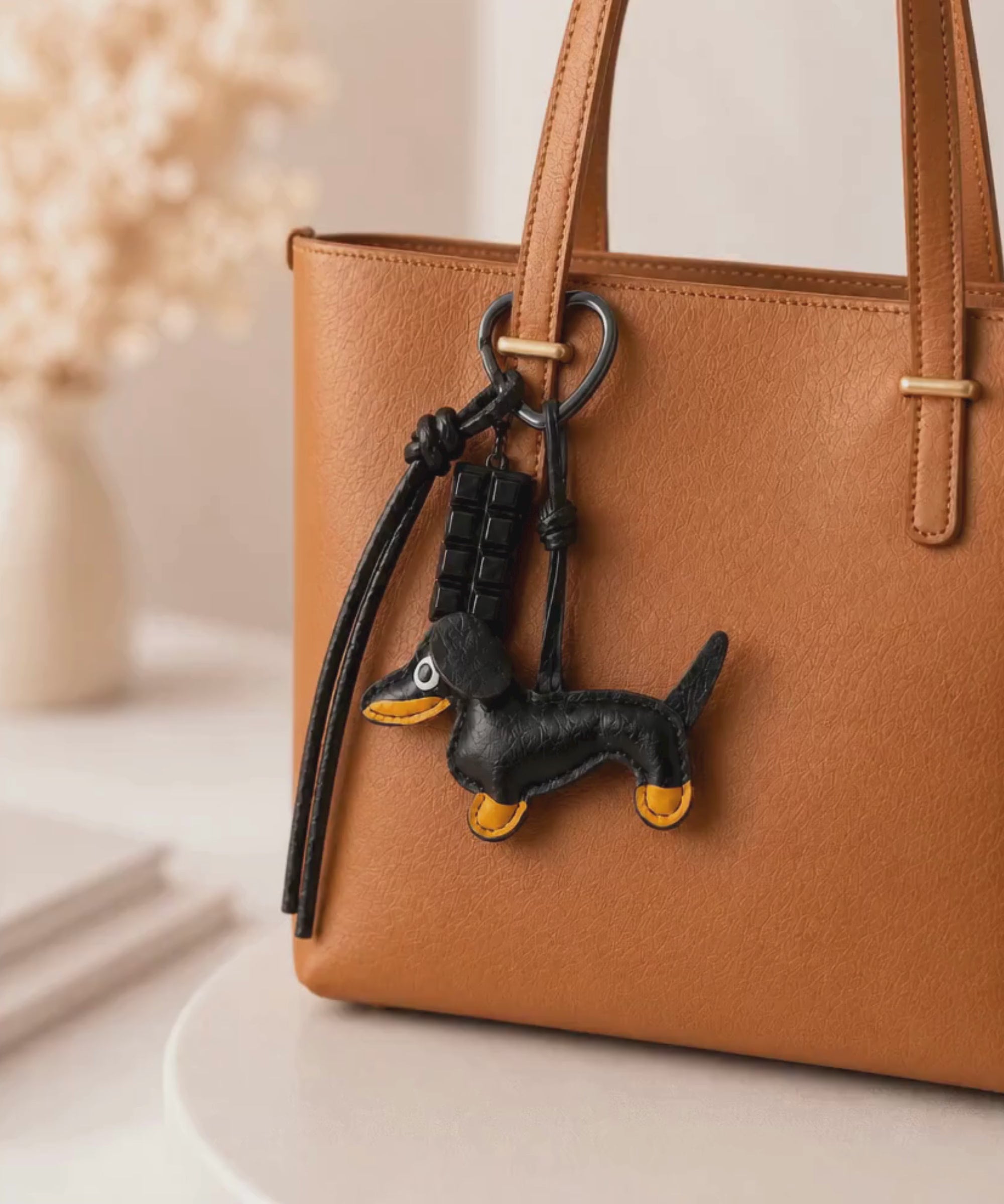 Black sausage dog PU leather bag charm keychain with a chocolate charm attached to a handbag, shown in a lifestyle video with the bag being lifted.