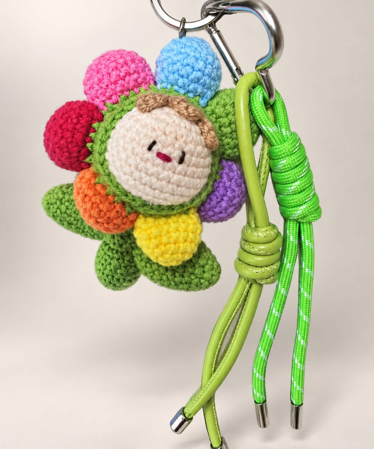 Colourful rainbow flower crochet keychain with smiling centre and green leaves